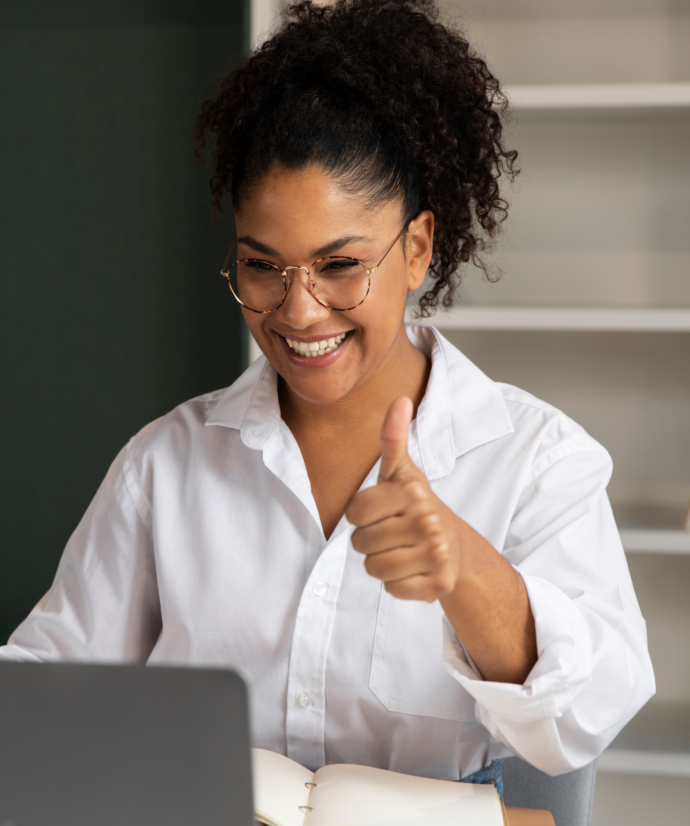 Smiling woman giving a thumbs up while working on a laptop